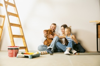 a young family sits on the floor of their home near a ladder and supplies used for remodeling a house