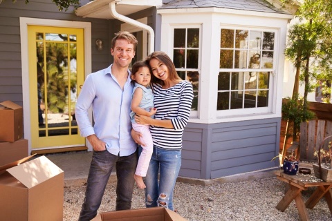 couple and young girl with moving boxes outside home