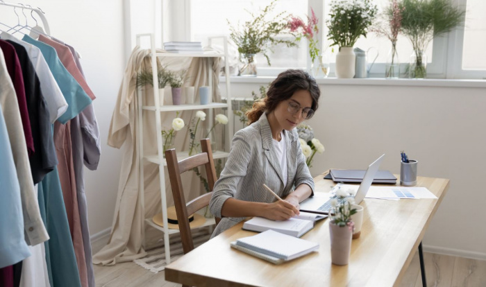 Caucasian female designer working on a laptop and making notes
