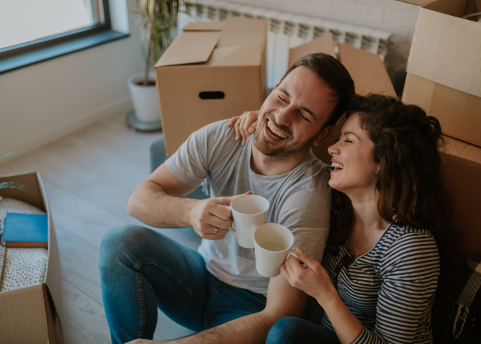 Top view photo of young happy couple drinking water while cardboard boxes are all around them. Young couple is moving in to their new home.