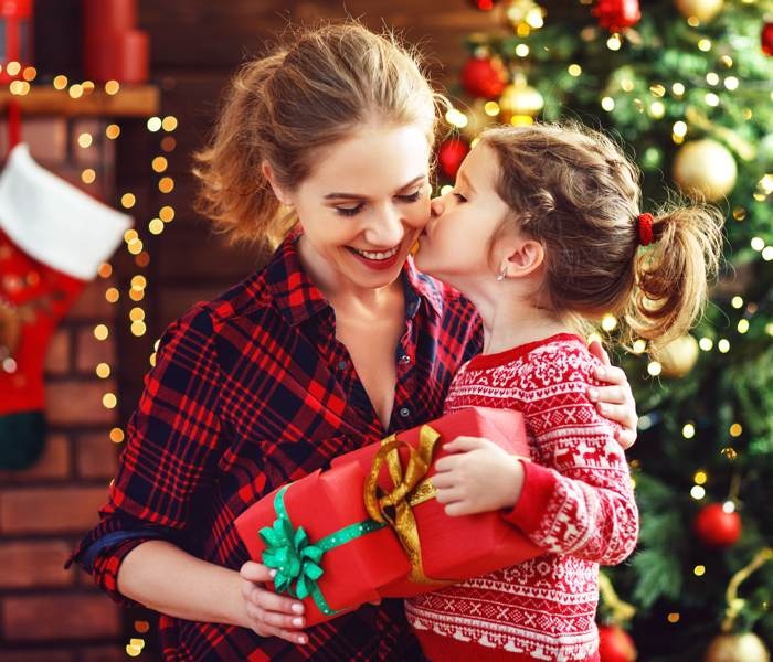 mother daughter with wrapped gift in front of holiday tree with ornaments