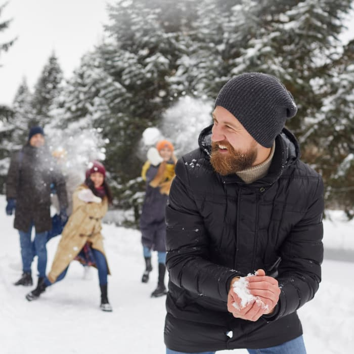A man wearing a coat and a beanie preparing to throw a snowball