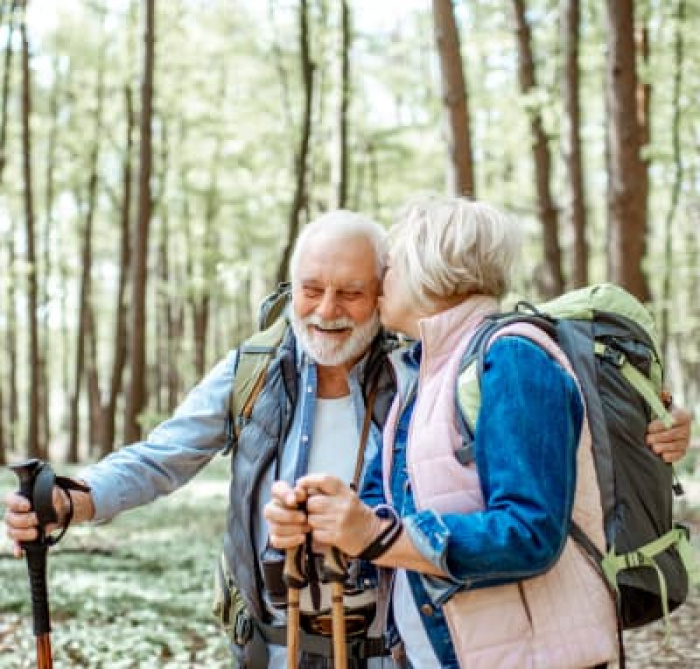 Beautiful senior couple hiking with backpacks and trekking sticks in the forest.