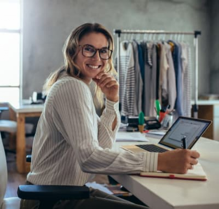 A woman working smiling while working at a desk and writing in her notebook