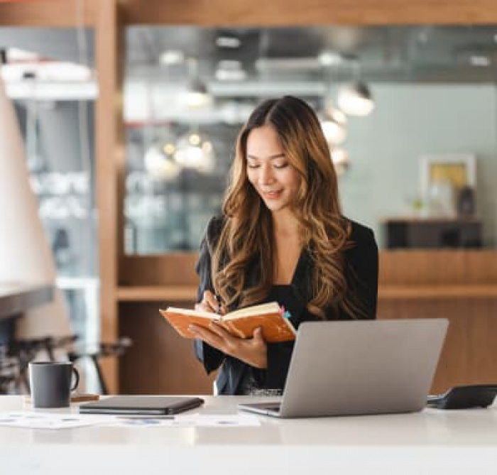 A woman sitting at her laptop while writing in a notebook