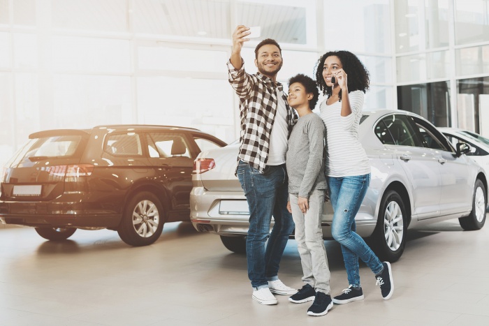 a family choosing a car at the dealership and taking a selfie in front of their new vehicle