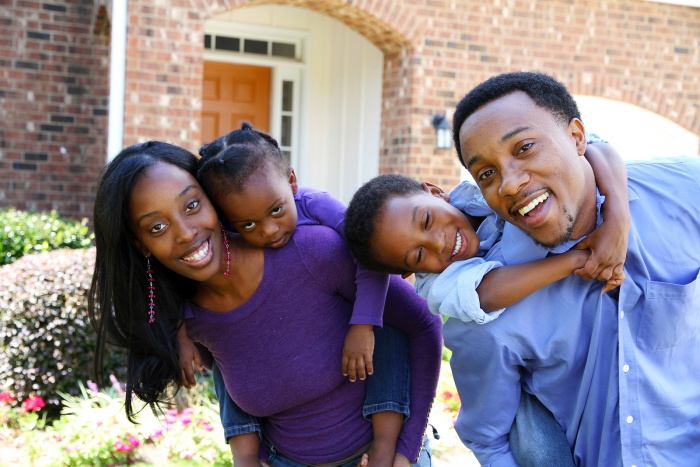 a happy family outside of their home, mother and father both have a child on their back