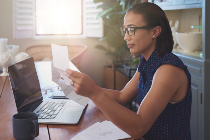 young woman looking at papers in front of her laptop