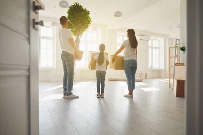 parents and their young daughter carry boxes into their new home