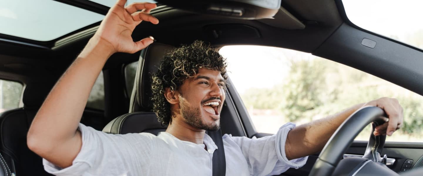 An African American man driving with his arm raised and the window open
