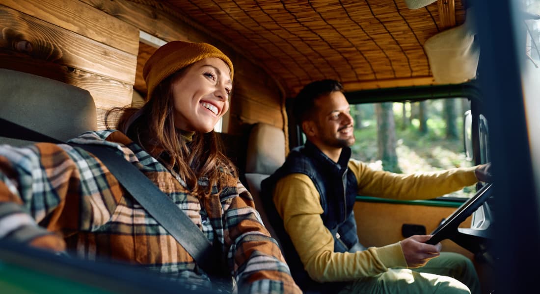 Happy woman and her boyfriend riding in their travel van through nature.