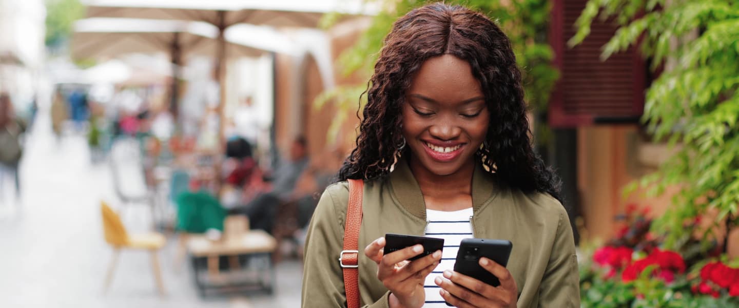 Waist up portrait view of the multiracial woman holding credit card and typing details at her smartphone
