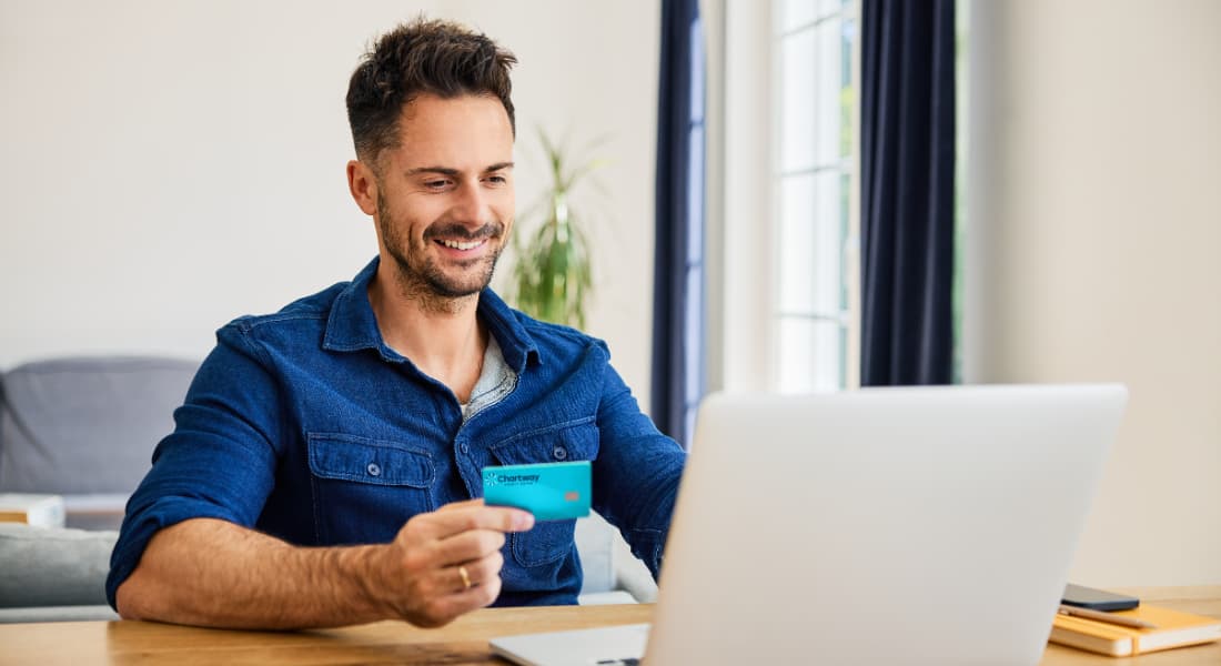 Man holding Chartway Signature Rewards card while working on his laptop